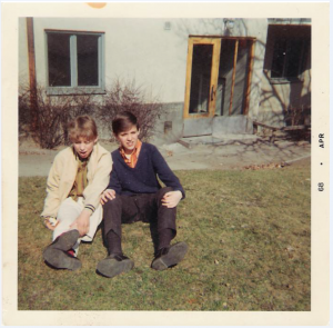 Bild från gården en vårdag år 1968. Kompisarna Olle Sålder och Peter Nyström, båda i trean njuter av solen. Olle vann SM i gymnastik. Han brukade träna i både i brandstationens och Råsundaskolans gympasalar. Hans pappa var flygstyrman på SAS långlinjer över Atlanten. Fotot visar också Vårvägen-fastighetens originalfärg som var gråvitt ända fram till första halvan av 1980-talet. Foto: Kodak Instamatic-kamera, april 1968.